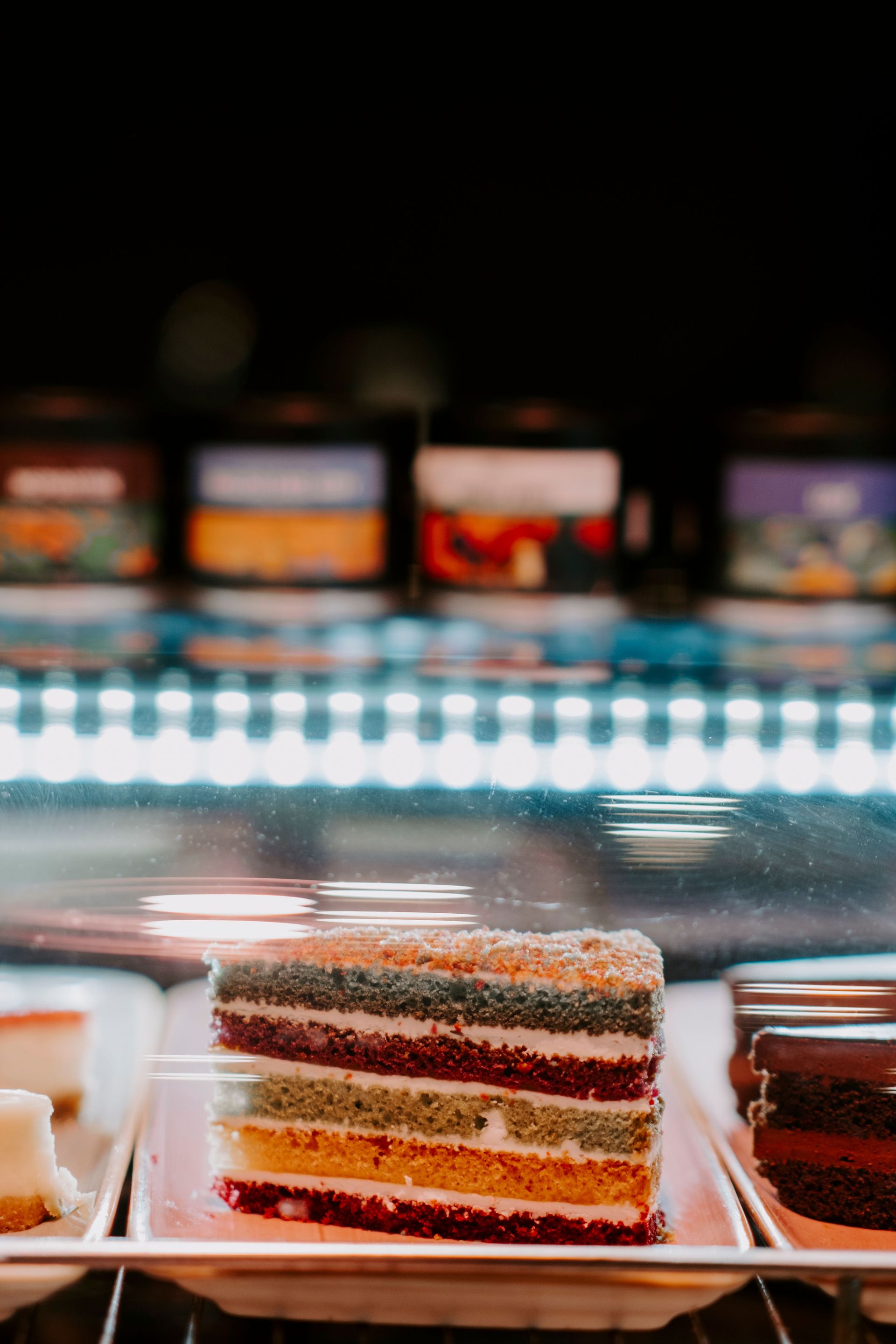 A vibrant multi-layered cake slice on display in a bakery.